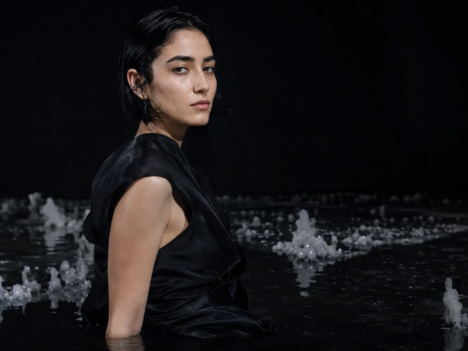 Mira Silt in a mineral-black flooded studio with salt bloom and a red light signal.