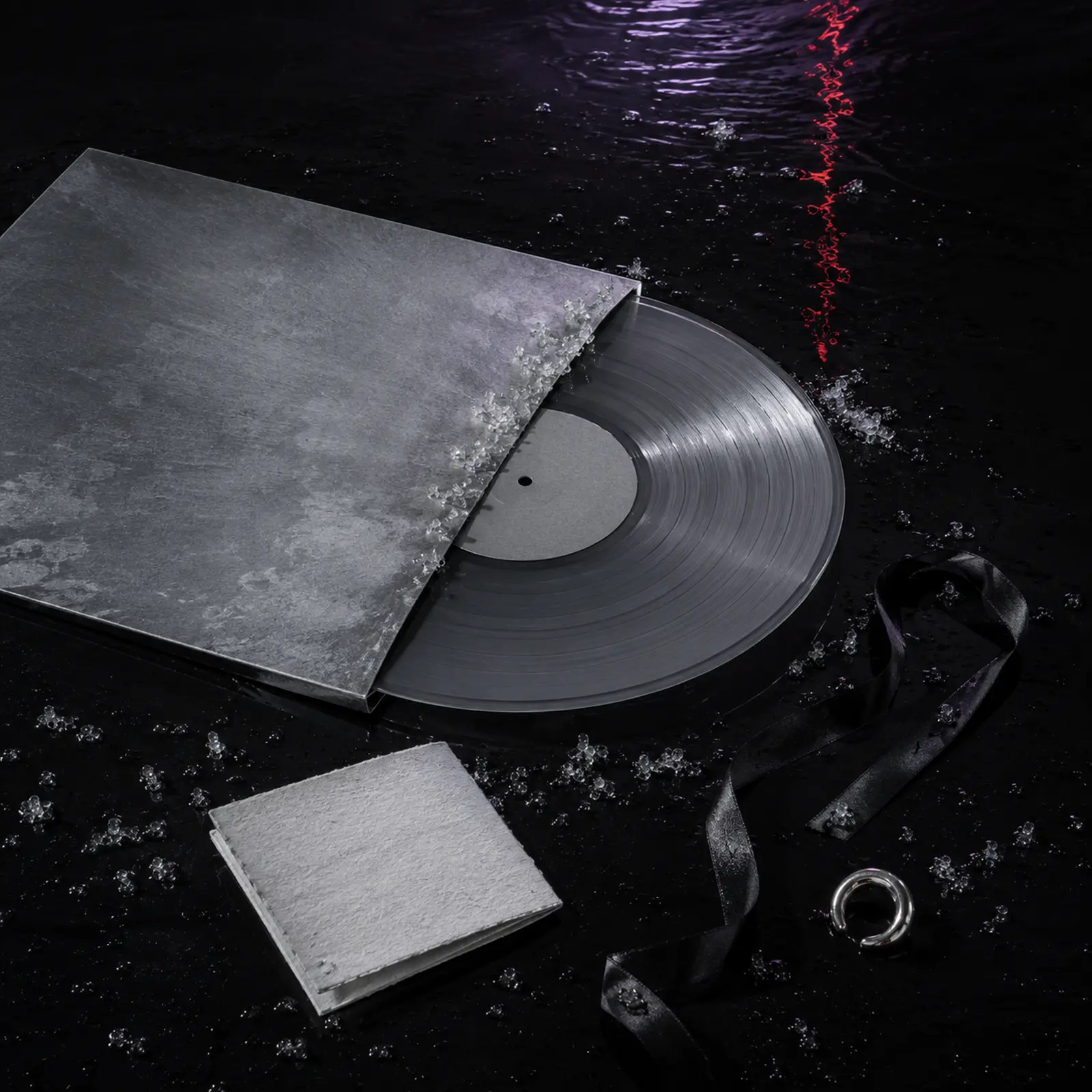A blank oxidised-silver record sleeve, smoke-grey vinyl and salt-paper booklet on wet black lacquer.