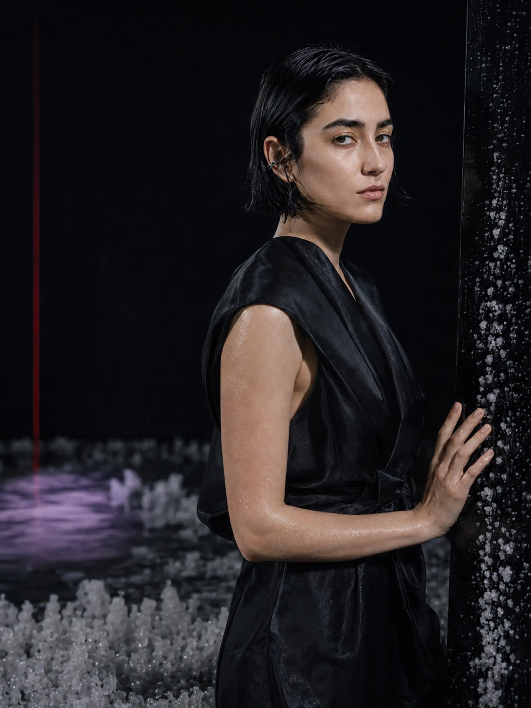 Portrait of Mira Silt in black silk beside a salt-covered piano-black surface.