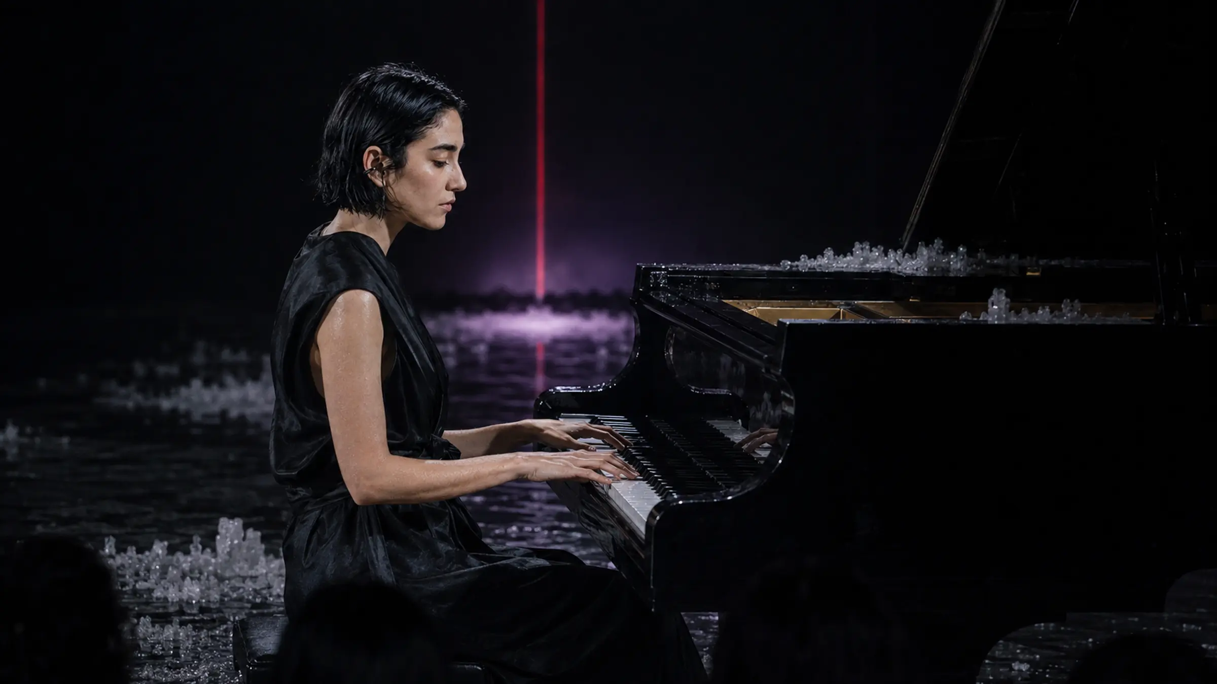 Mira Silt performing at a black grand piano on an intimate flooded stage.