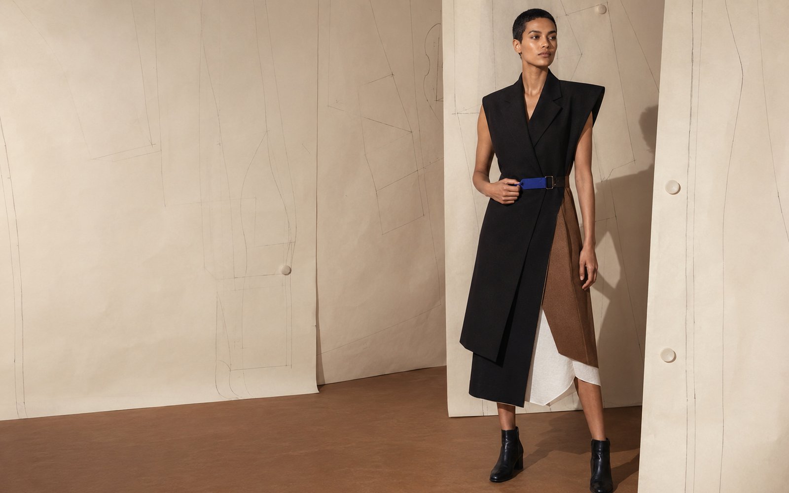 Ninth Form model wearing an asymmetric black, bone and tobacco modular look in a pattern-paper studio.